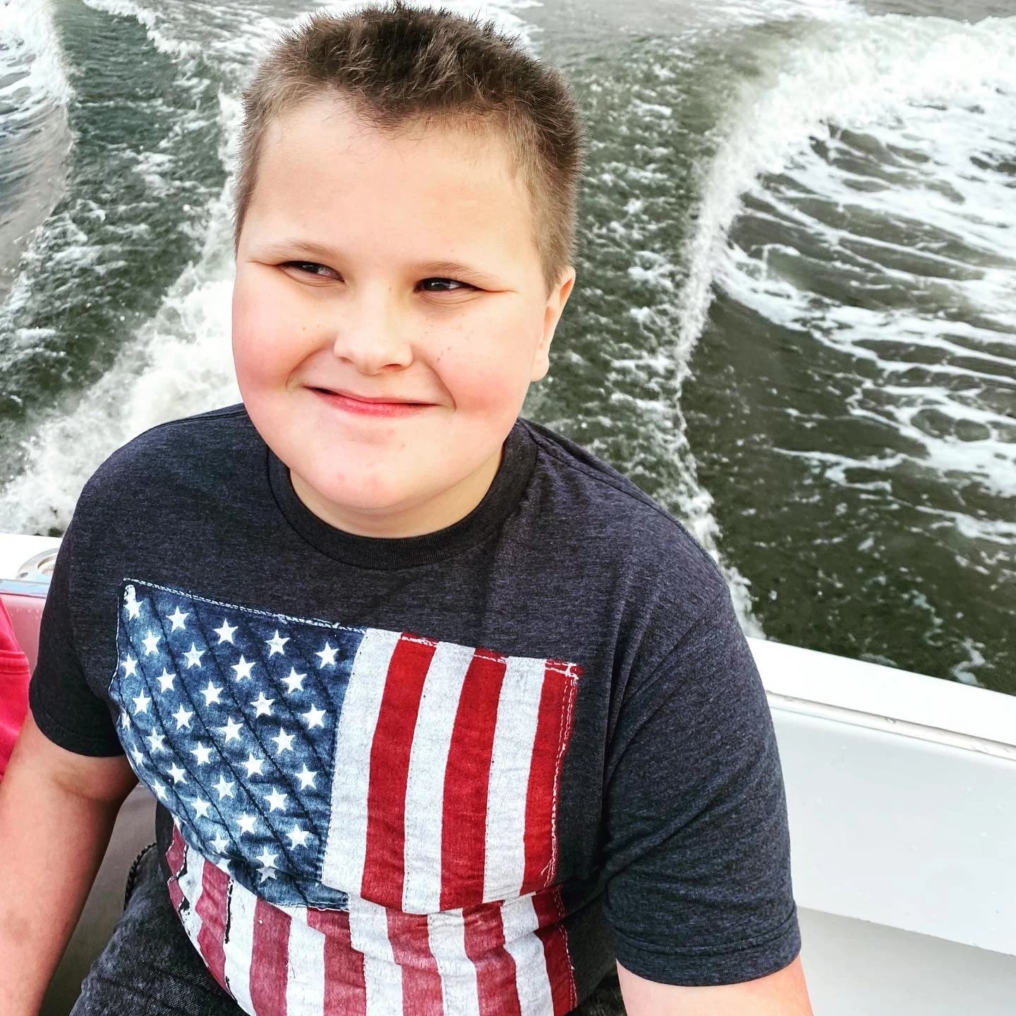 Parker smiling aboard a boat during a family outing in 2021, with the vessel’s wake behind him.